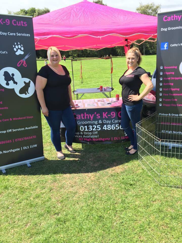 Two members of the team standing at the pink Cathy's K-9 Cuts gazebo at an outdoor event